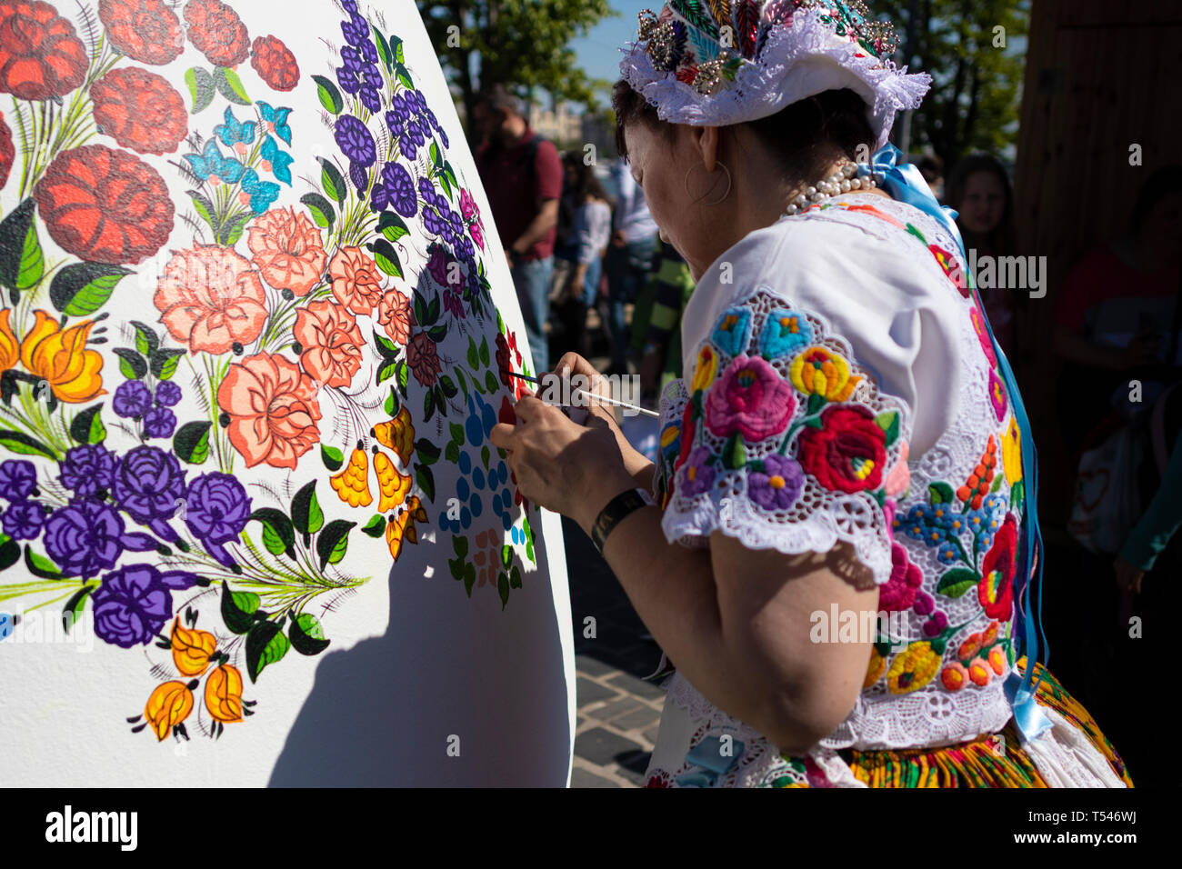 BUDAPEST/HUNGARY - 04.21.2019: A giant white Easter Egg is being decorated with folklore floral patterns by a young woman wearing traditional Hungaria Stock Photo