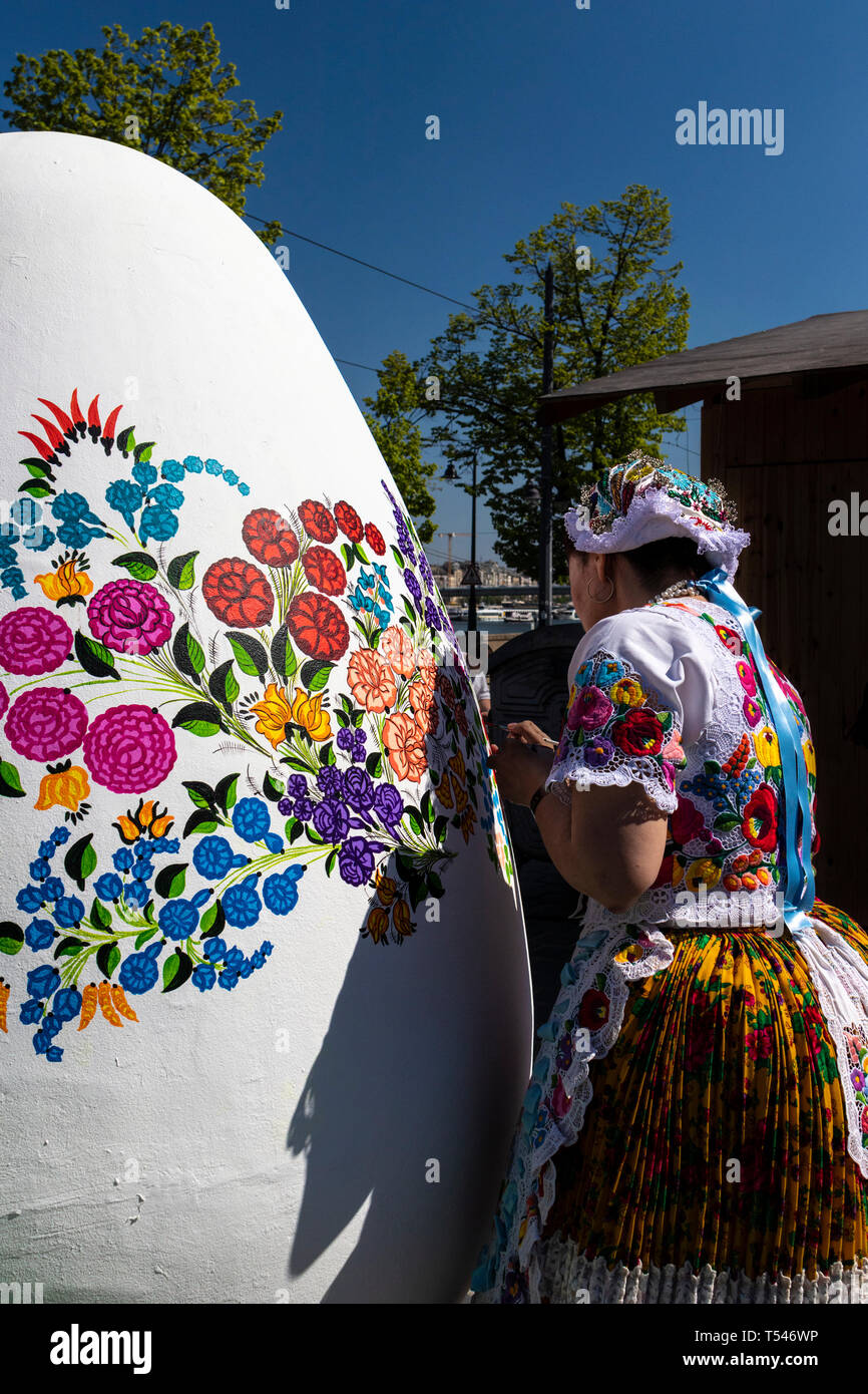 BUDAPEST/HUNGARY - 04.21.2019: A giant white Easter Egg is being decorated with folklore floral patterns by a young woman wearing traditional Hungaria Stock Photo