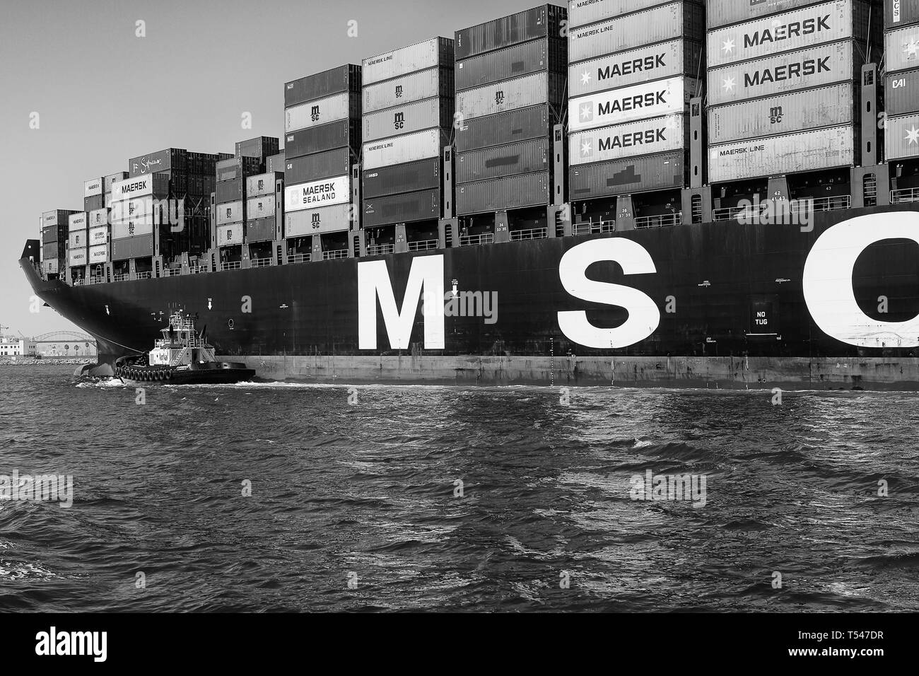 Black And White Photo Of The Container Ship, MSC ELODIE, Escorted By Tugs, Underway Towards The Long Beach Container Terminal, California, USA. Stock Photo