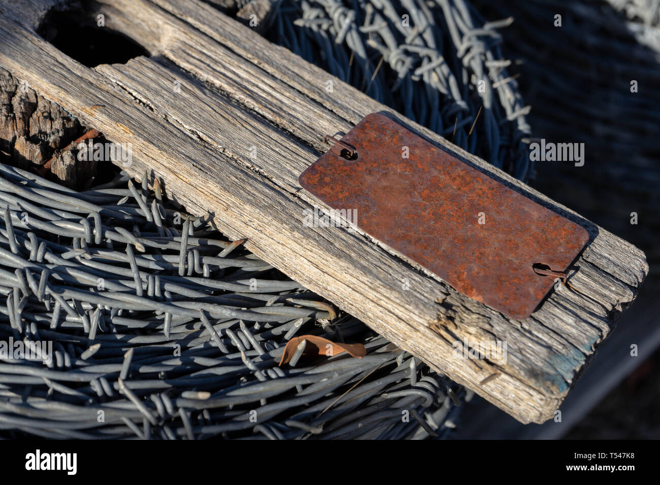 Roll of barbed wire on an old piece of wood with a rusted metal tag ...