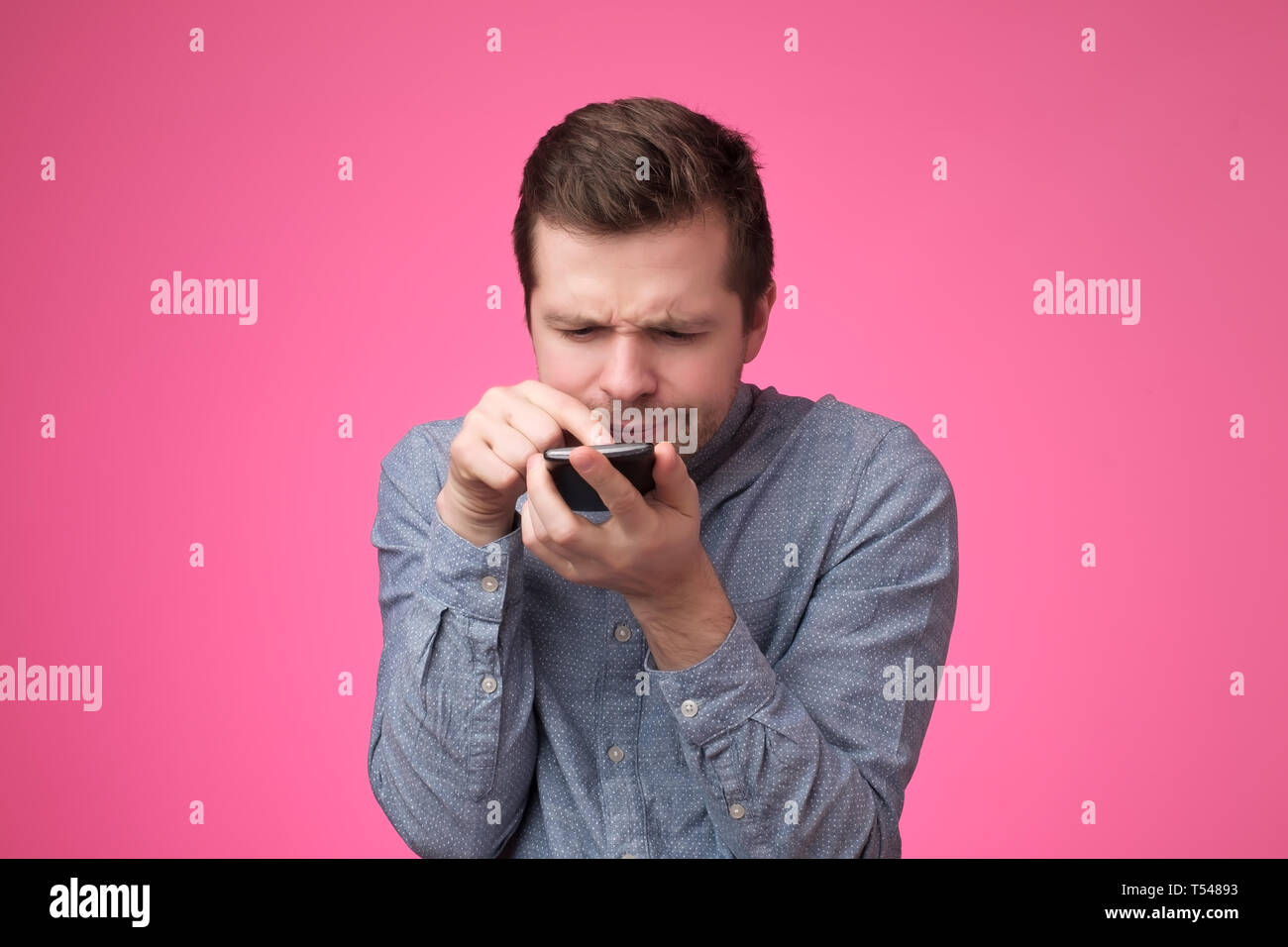 young man standing, using smartphone and watching video with amazed face. Stock Photo