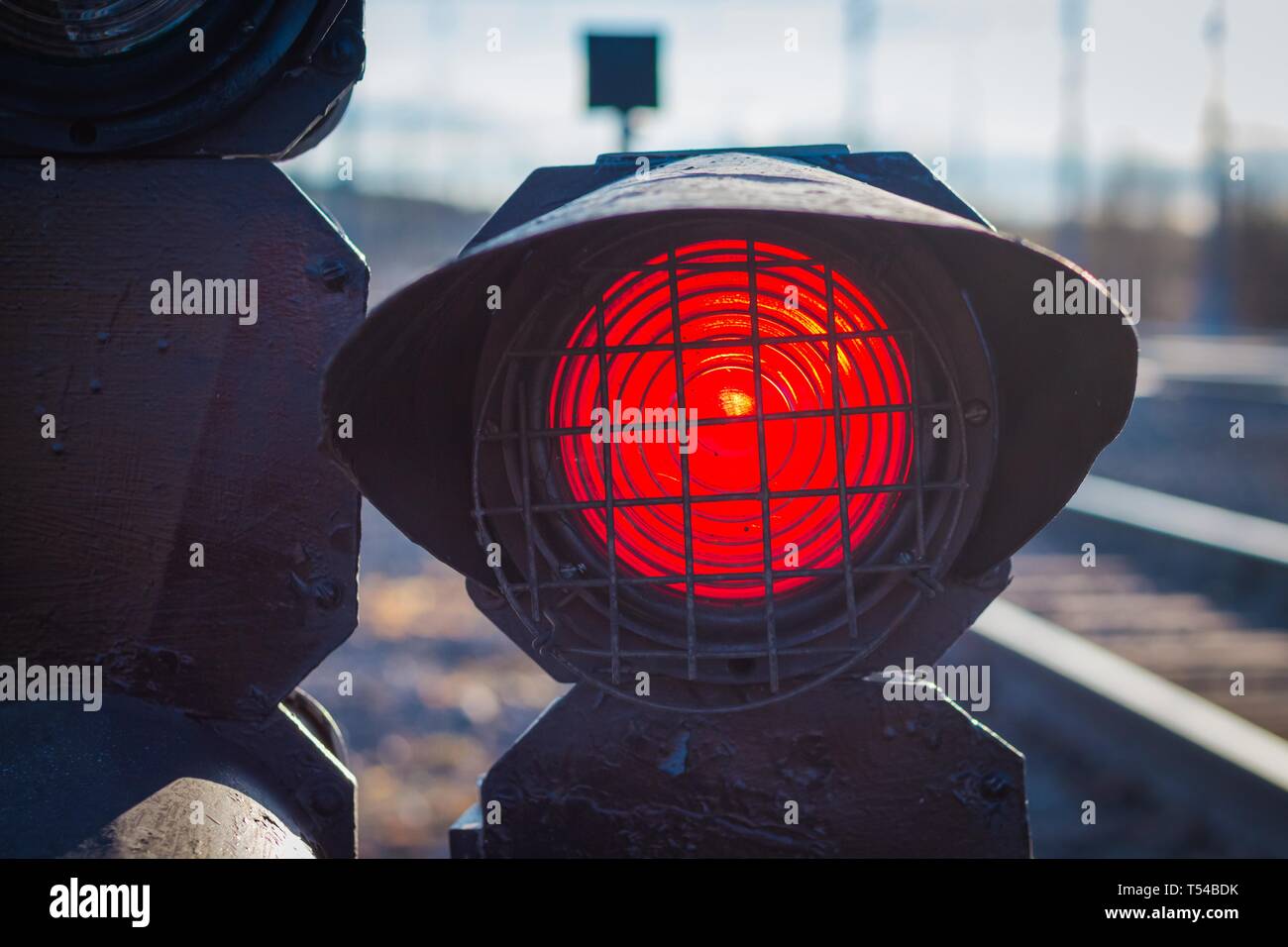 There is a traffic light on the railway for warning of train movement. The traffic light is lit in red warning of the approaching train. Stock Photo