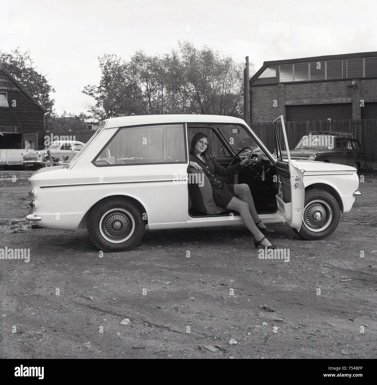 1967, historical, young  lady wearing a woollen cardigan and skirt sitting in the drivers seat of a Sunbeam Sport motorcar,  the sports version of the famous small car, the HIllman Imp. The Hillman Imp was a small car made by Rootes Group and  its successor Chrysler Europe from 1963 until 1976 was the competitor in the small car category to the Mini. Stock Photo