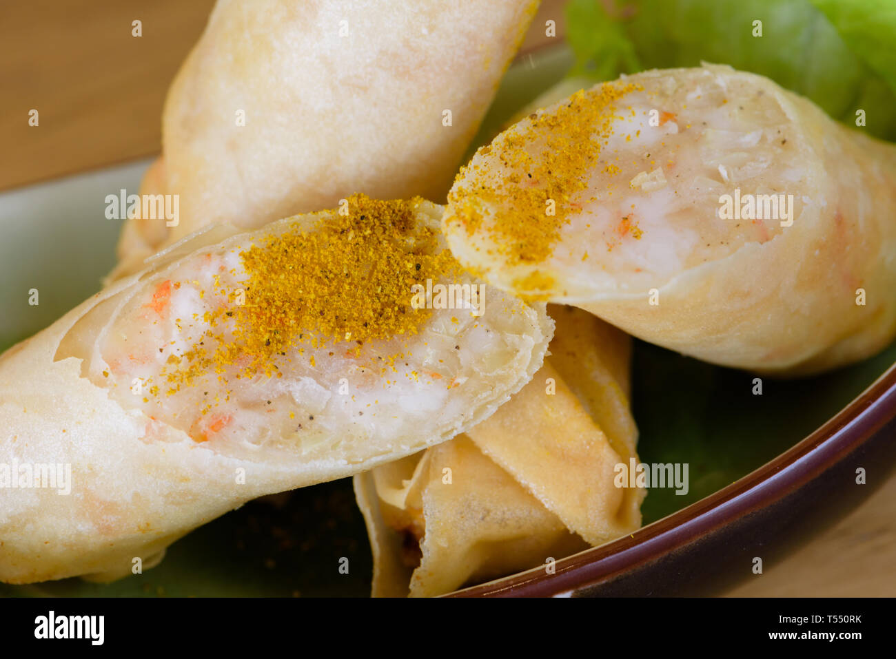 Harumaki, fried rolls in batter with shrimp pulp, flavoured with paprika, served with green salad on a boat-shaped plate, wooden table background - Im Stock Photo