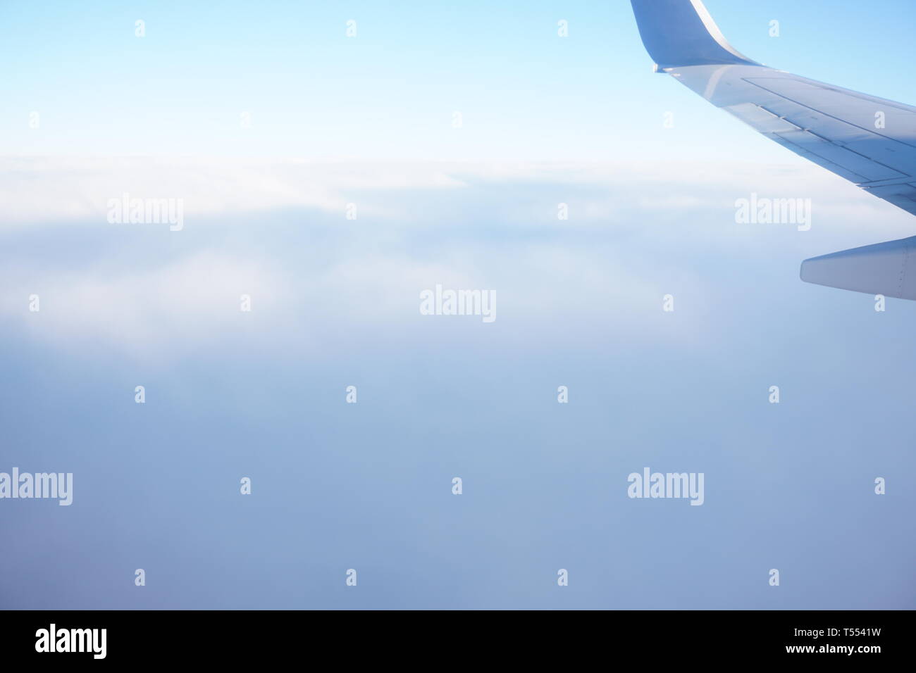 Airplane wing from airplane window above the clouds in the sky. Stock Photo