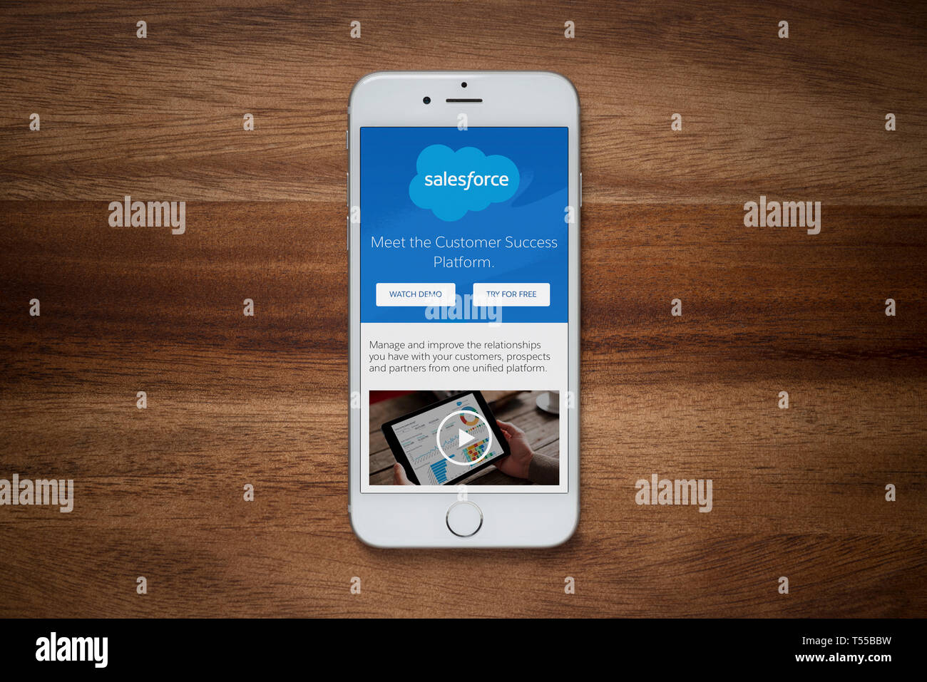 An iPhone showing the Salesforce website rests on a plain wooden table (Editorial use only). Stock Photo