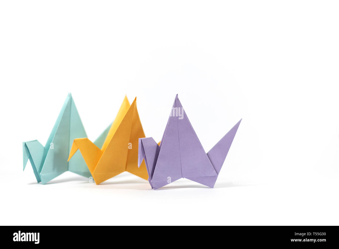 Three hand folded pastel coloured origami paper cranes, standing isolated on a white background