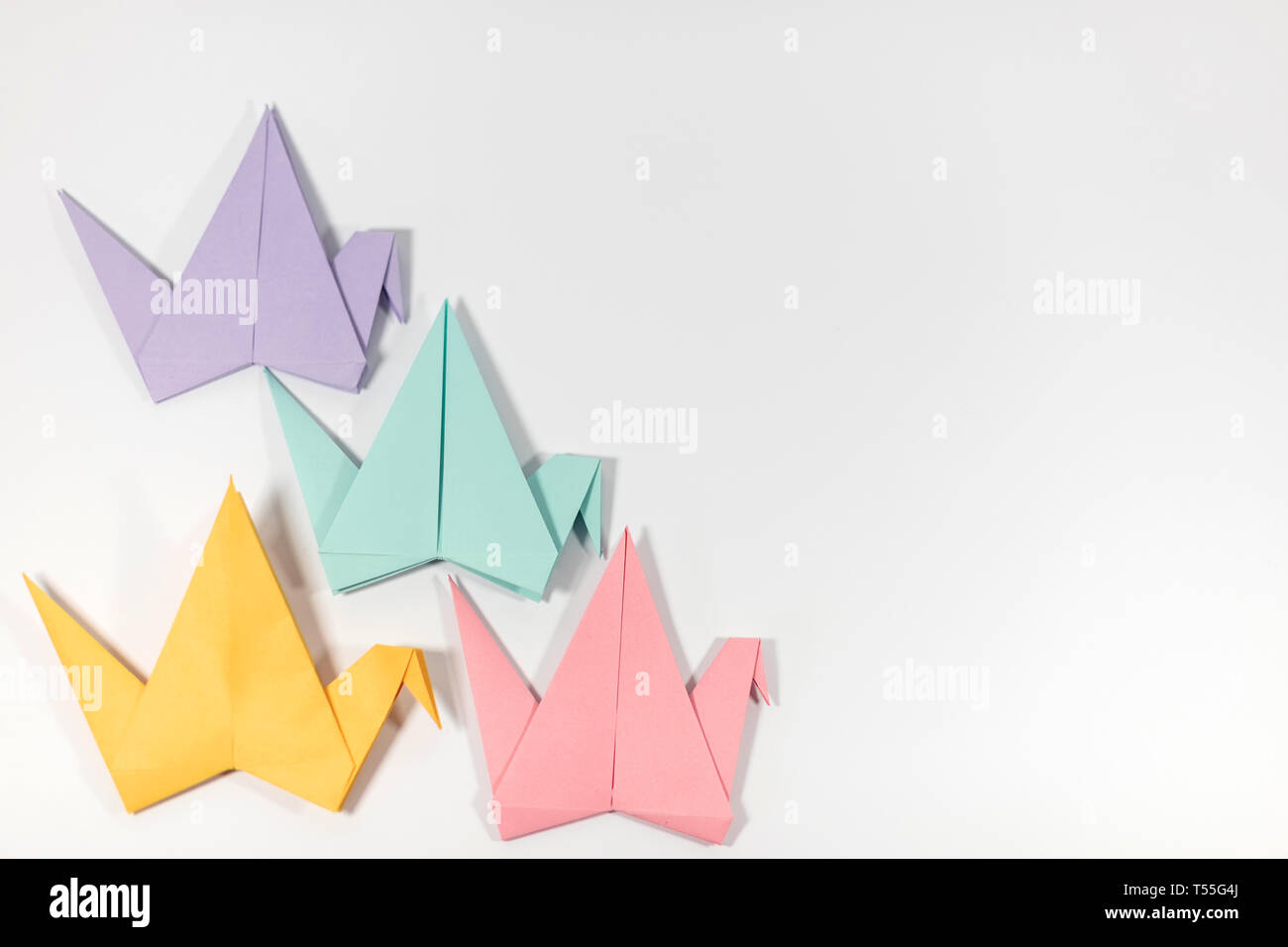 Four hand folded pastel coloured origami paper cranes arranged in a pattern, isolated on a white background Stock Photo