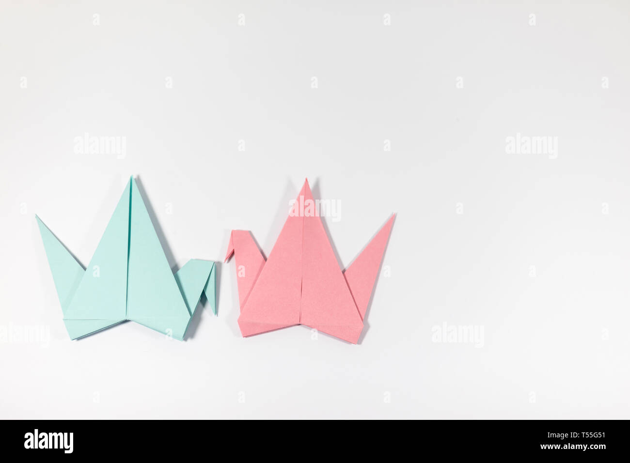 Two hand folded pastel coloured origami paper cranes facing each other, isolated on a white