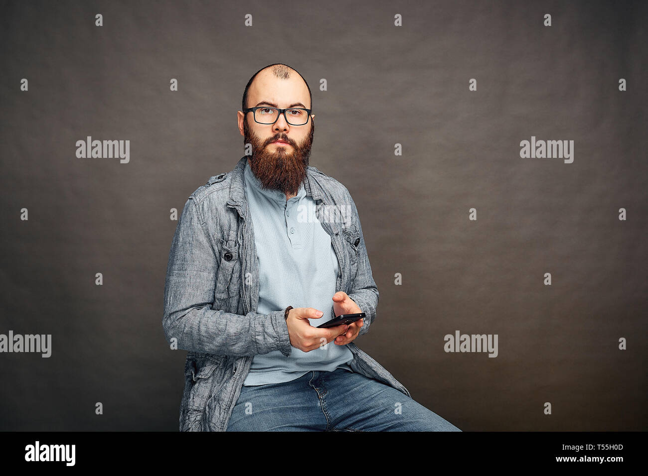 bearded man in glasses with phone in hand on brown background. Stock Photo