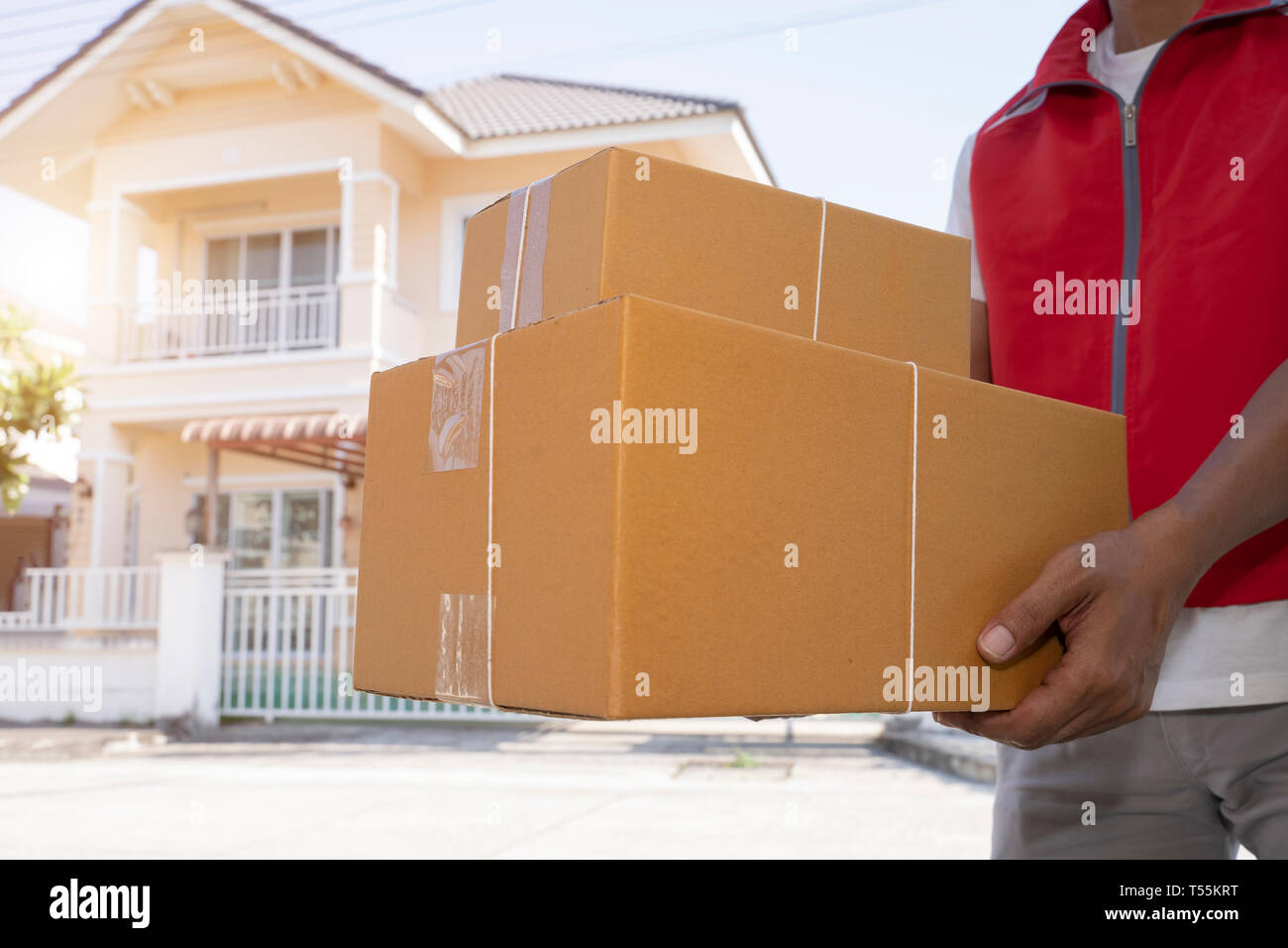 Delivery man in red uniform handing parcel boxes to recipient - courier service concept - Image Stock Photo