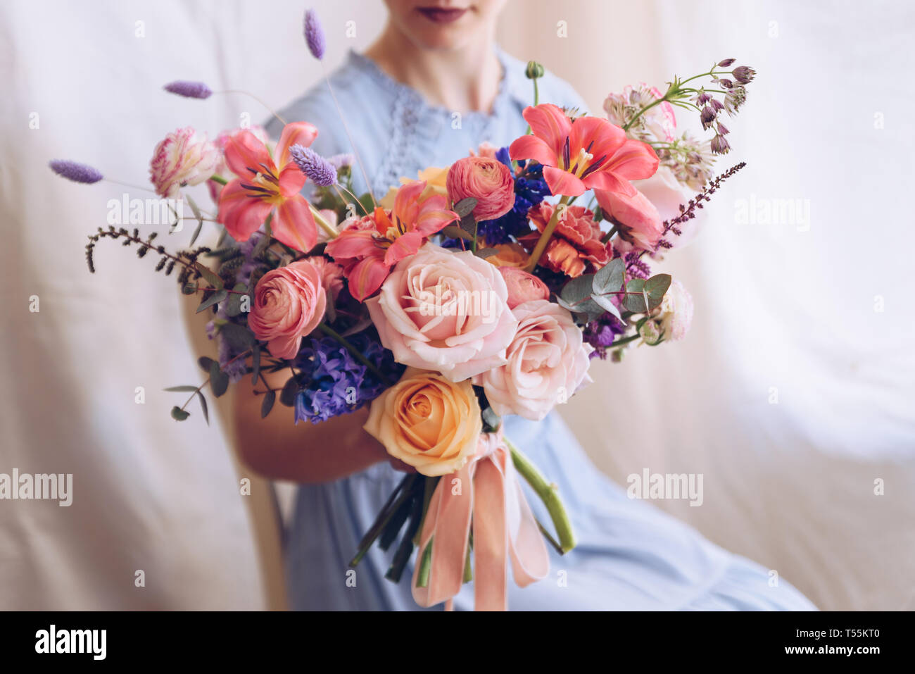 Young woman in a light blue dress holding a bouquet of flowers ...