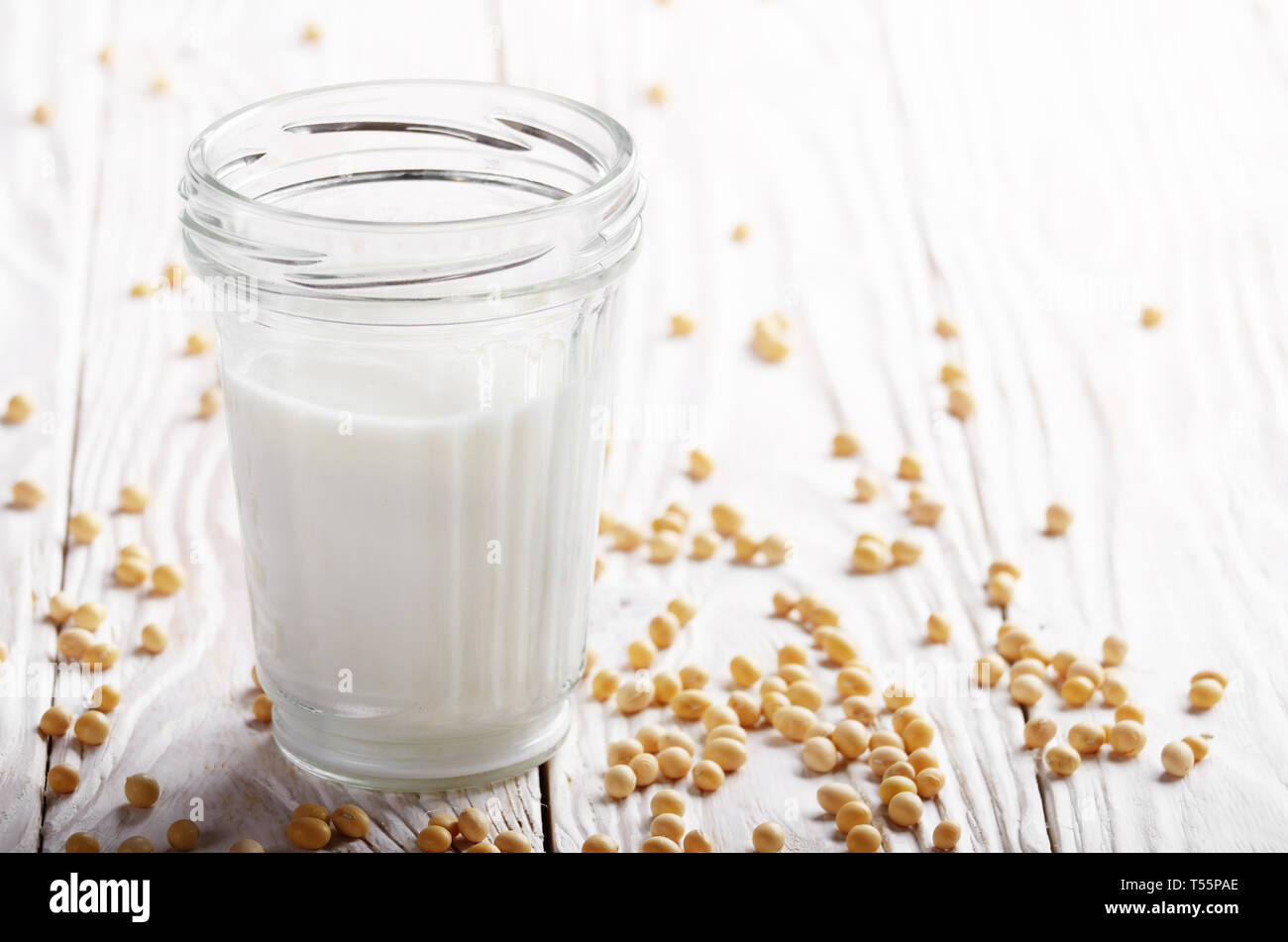 Non-dairy alternative Soy milk or yogurt in mason jar on white wooden table with soybeans aside Stock Photo