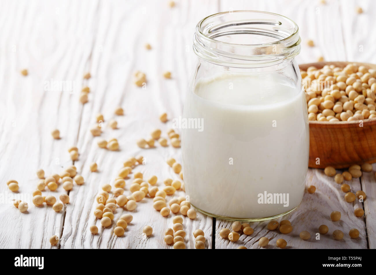 Non-dairy alternative Soy milk or yogurt in mason jar on white wooden table with soybeans in bowl aside Stock Photo