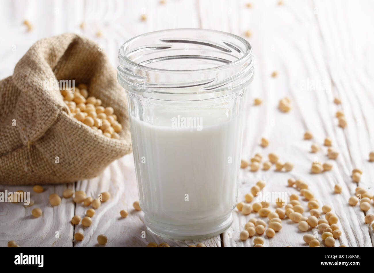 Non-dairy alternative Soy milk or yogurt in mason jar on white wooden table with soybeans in hemp sack Stock Photo