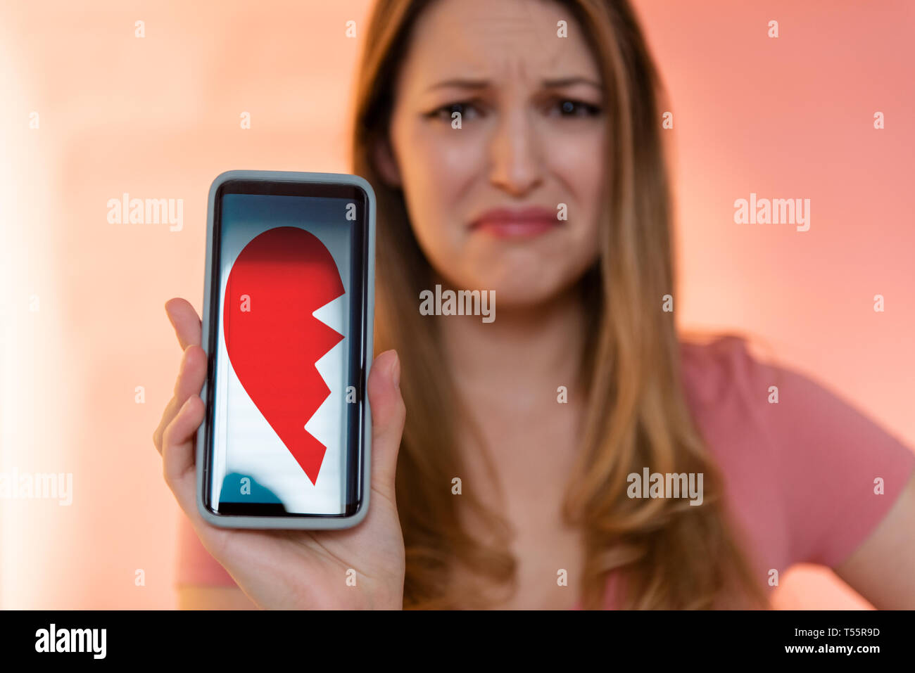 Young woman holding smart phone displaying broken heart Stock Photo