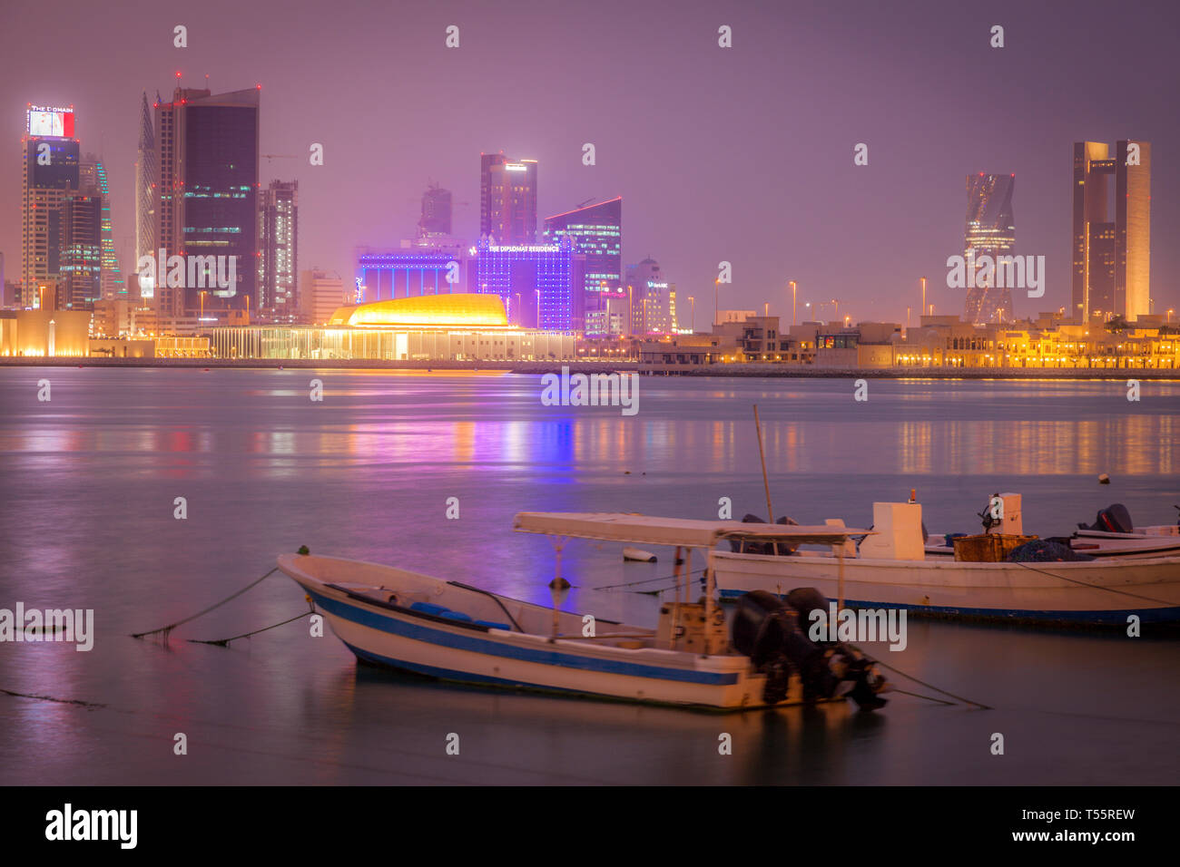 Moored motorboats by city skyline at night in Manama, Bahrain Stock Photo
