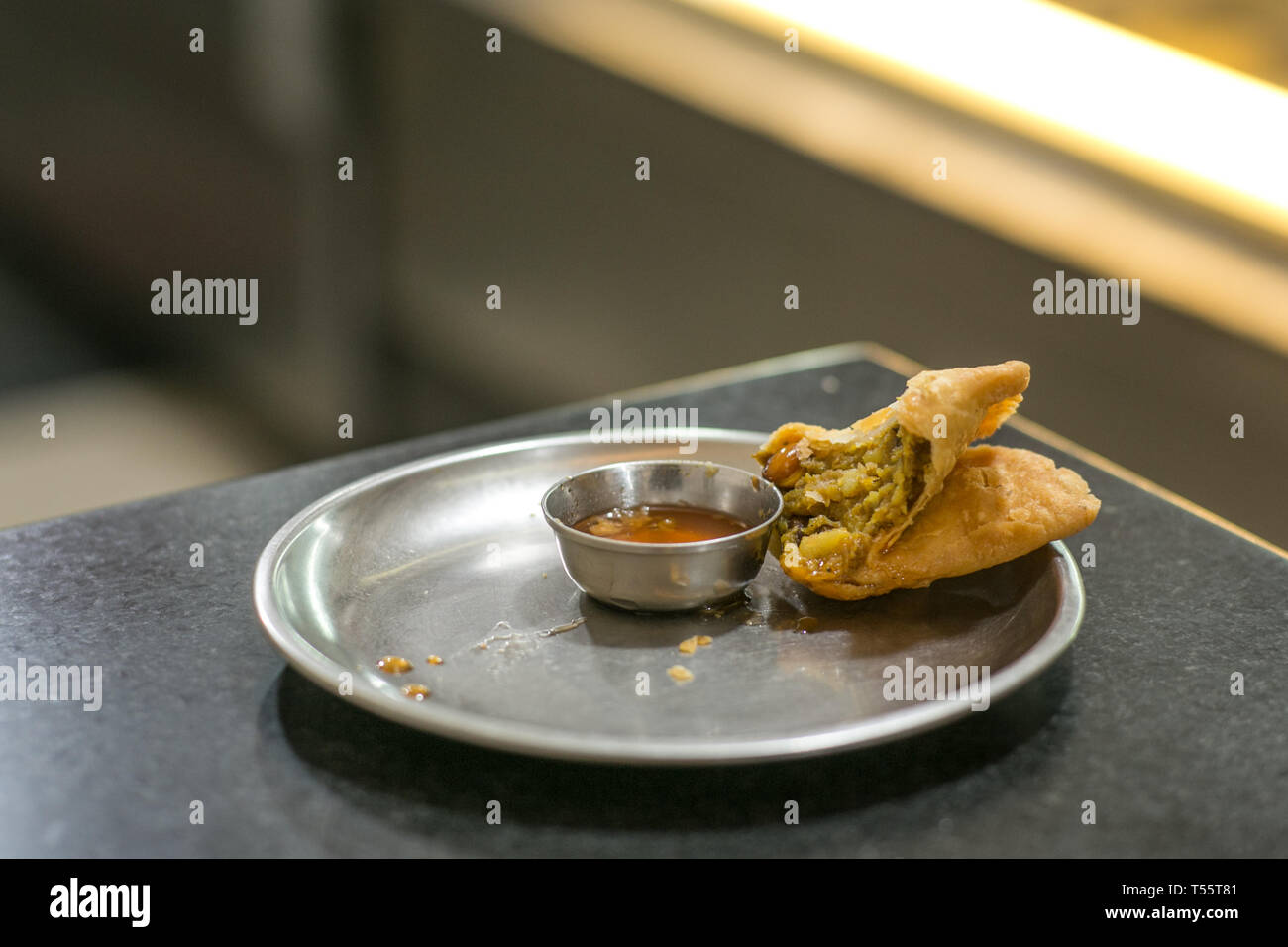 A peace of half eaten samosa on a plate in a restaurant Stock Photo