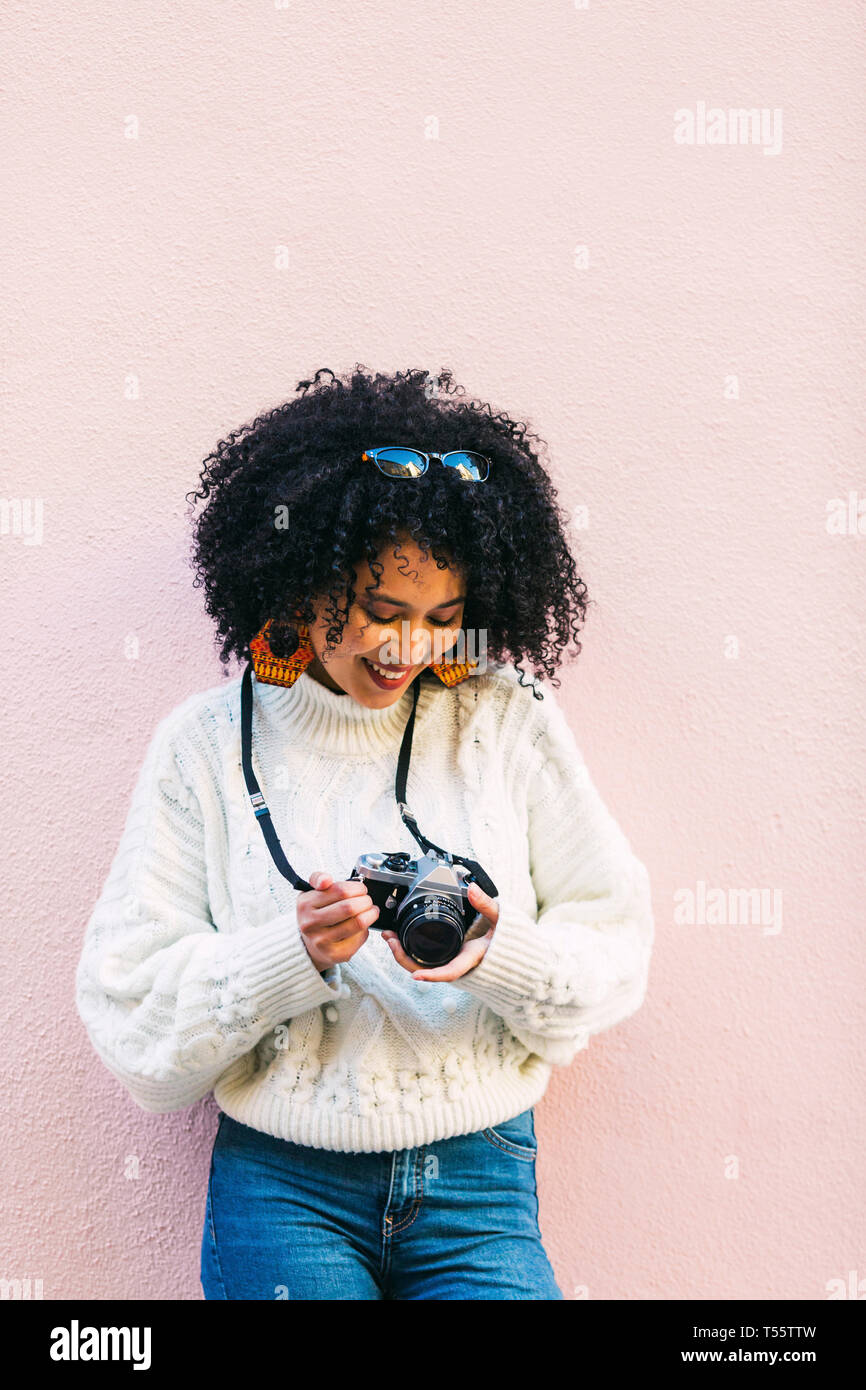 Young woman holding camera against pink wall Stock Photo - Alamy
