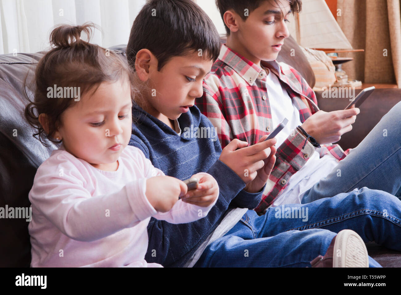 Siblings using smart phones on sofa Stock Photo