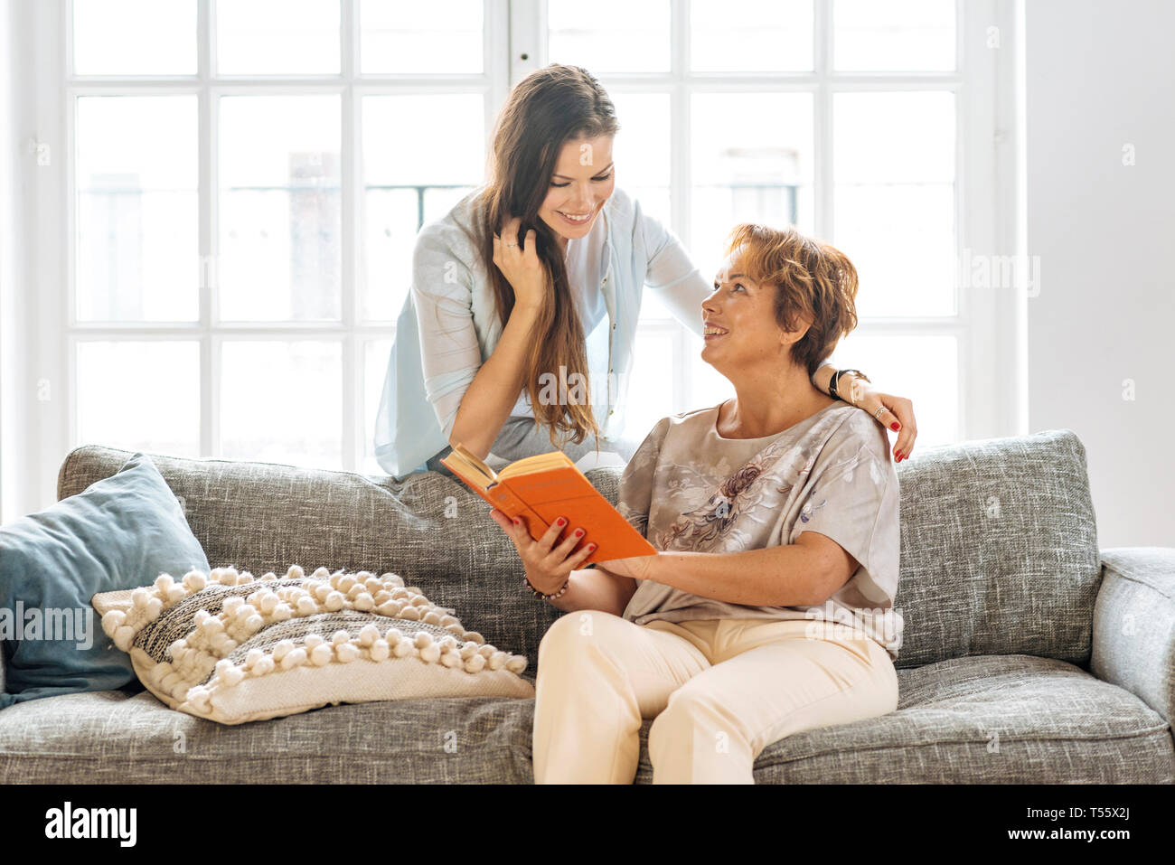 Mother and adult daughter looking at book on sofa Stock Photo
