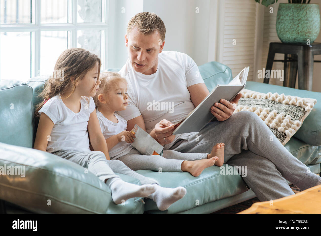Father reading book to daughters on sofa Stock Photo