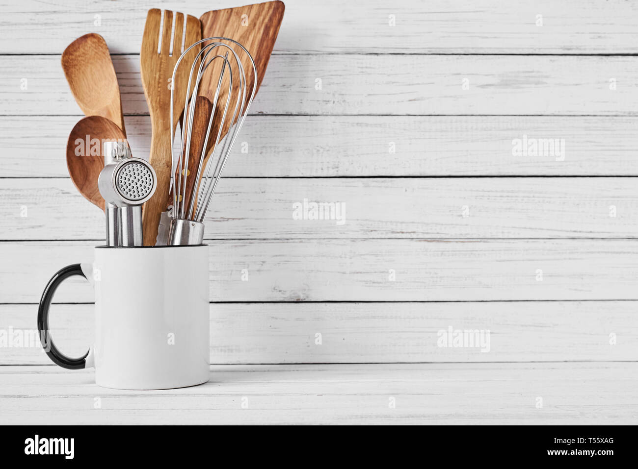 Cooking tools in ceramic cup on white background, copy space. Kitchen utensils background Stock Photo