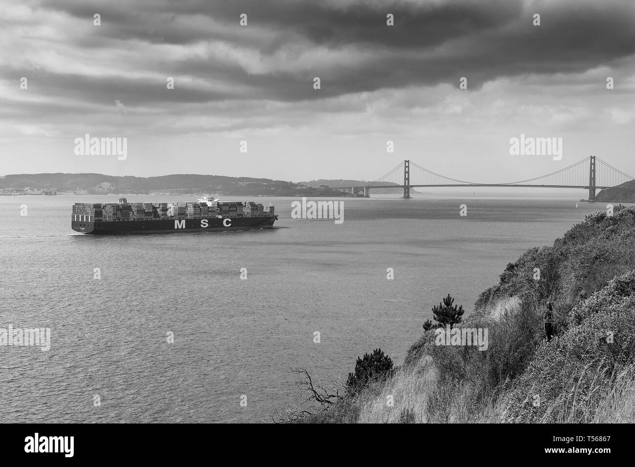 Moody Black and White Photo Of The Container Ship, MSC ARIANE, Steaming Through San Francisco Bay Towards The Golden Gate Bridge, California, USA. Stock Photo