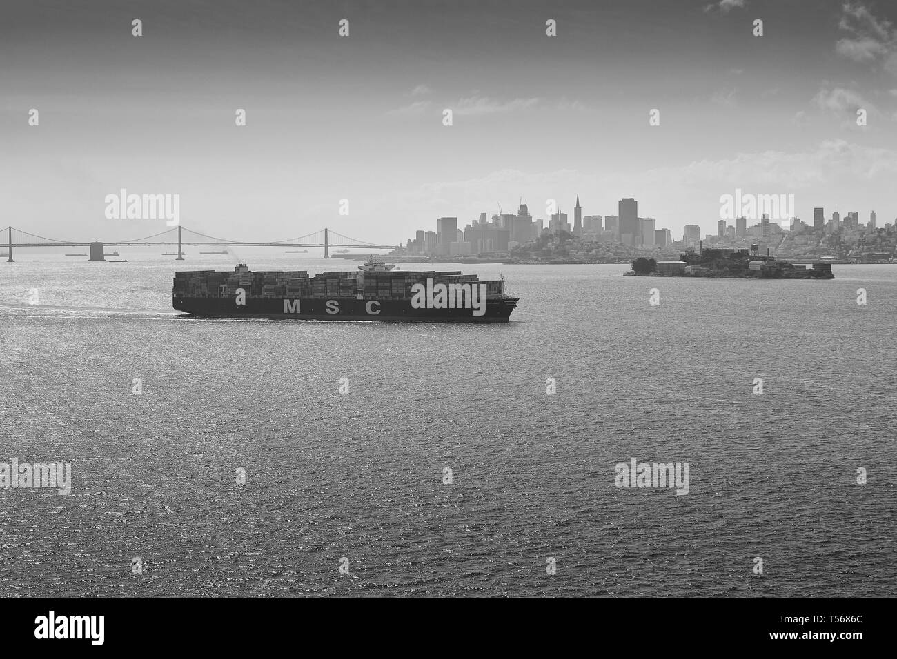 Black And White Photo Of Mediterranean Shipping Company Container Ship, MSC ARIANE, Steaming Through San Francisco Bay, San Francisco Skyline Behind. Stock Photo