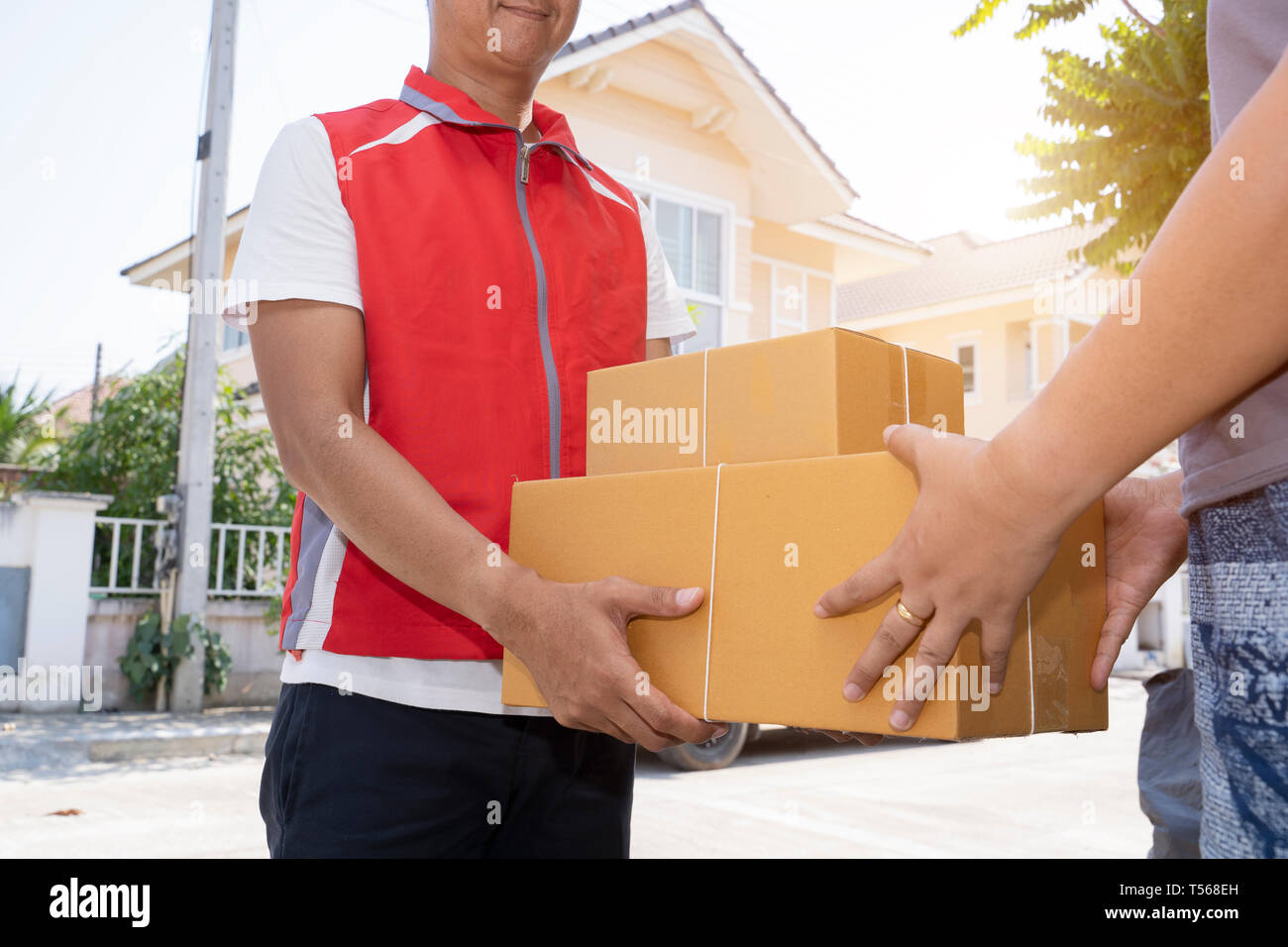 Delivery man in red uniform handing parcel boxes to recipient - courier service concept - Image Stock Photo