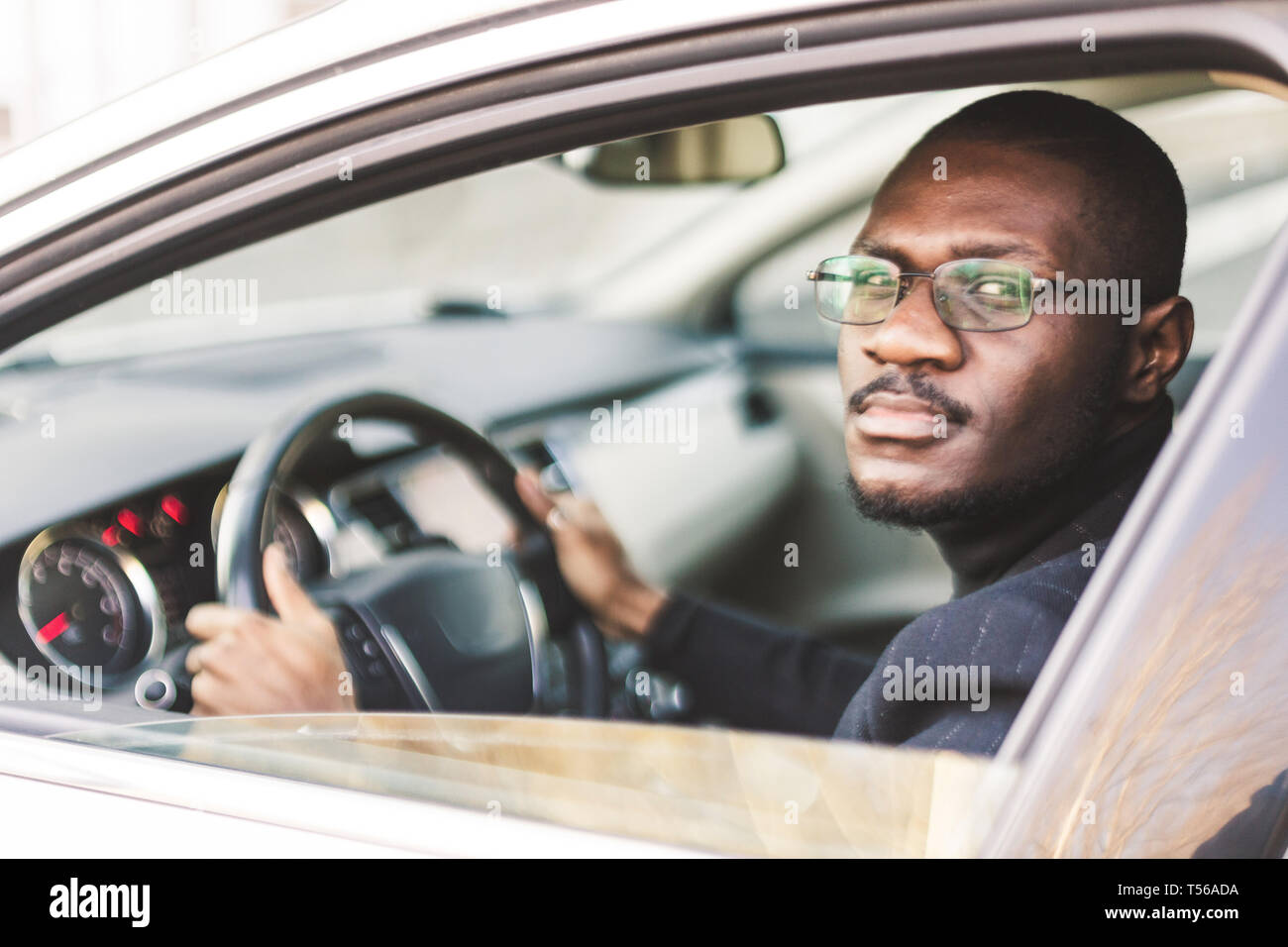 A young businessman in a suit sits at the wheel of a expensive car. Stock Photo