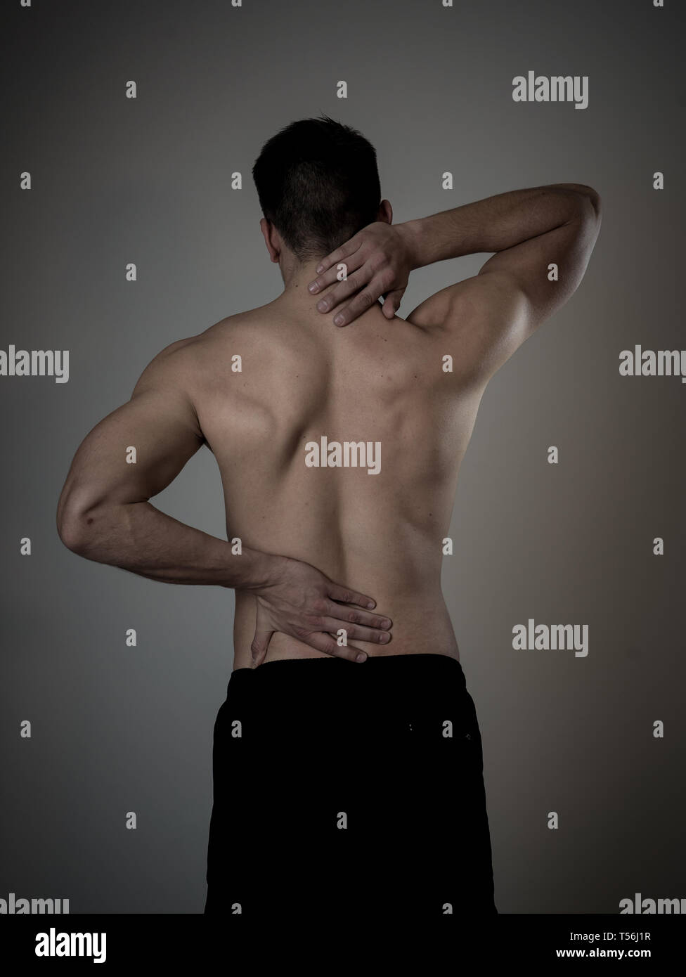 Young muscular fitness man touching and grabbing his neck and lower back suffering cervical pain isolated on neutral background. In sport and workout  Stock Photo