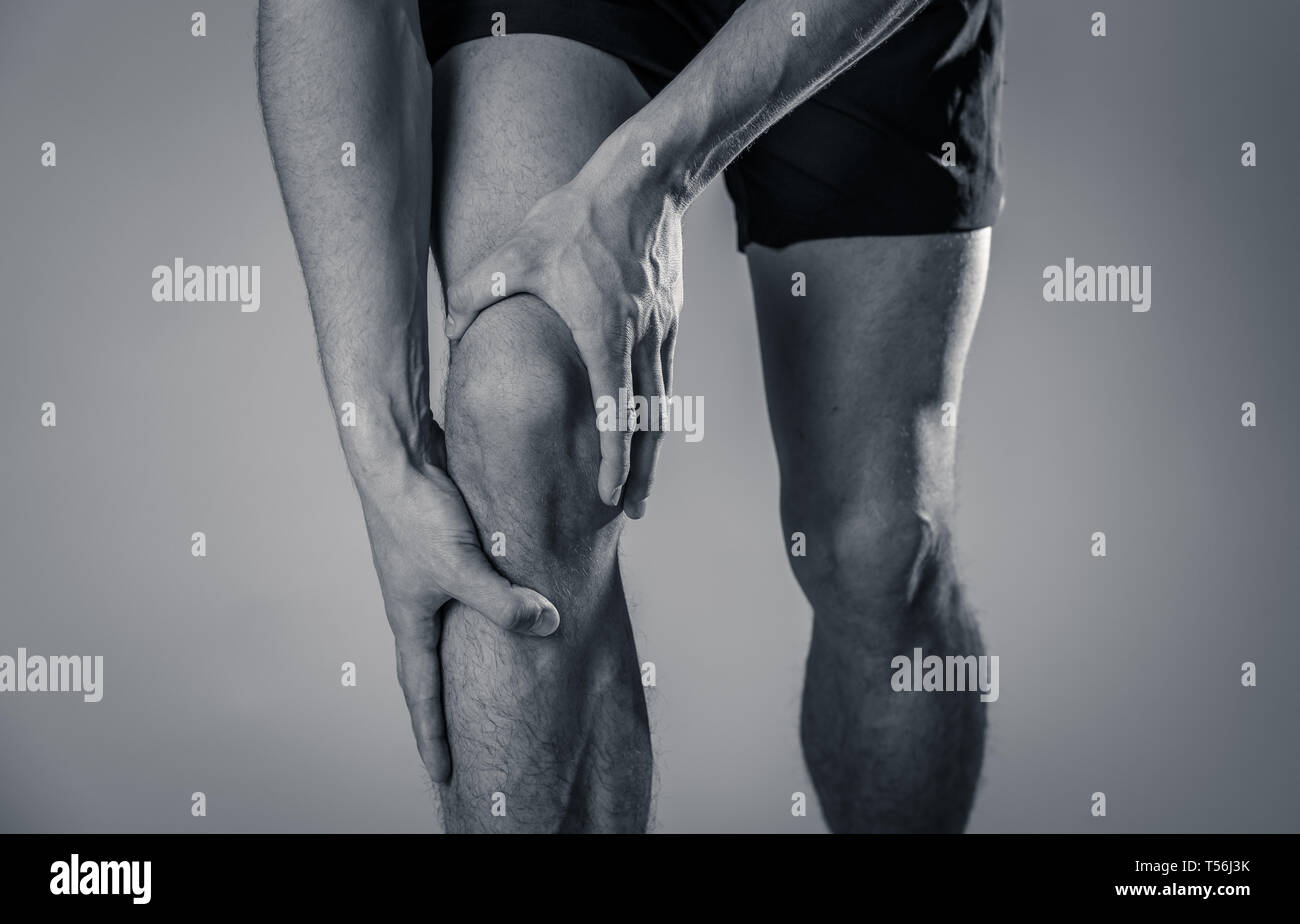 Young fit man holding knee with hands in pain after suffering muscle