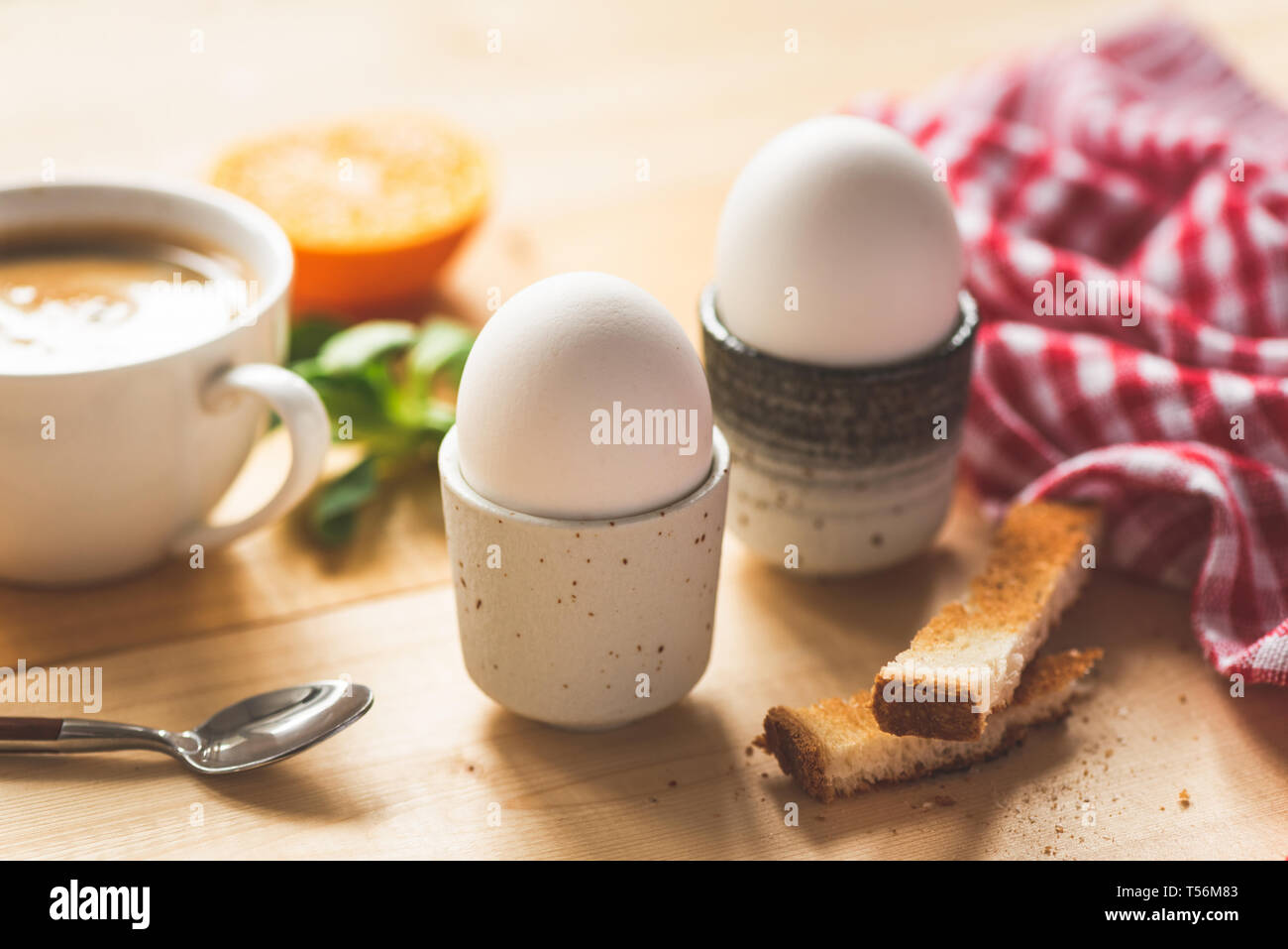 Boiled eggs for breakfast, cup of coffee, toasted bread and orange half. Healthy tasty breakfast on a wooden table. Closeup view, selective focus, ton Stock Photo