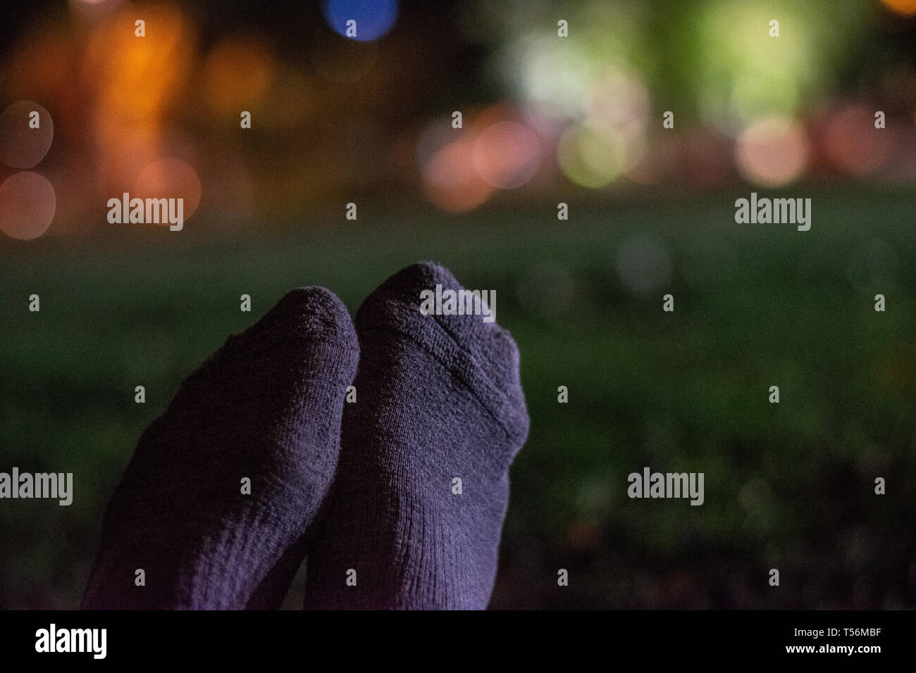 Socks on feet sitting in grassy park at night in urban city park Stock