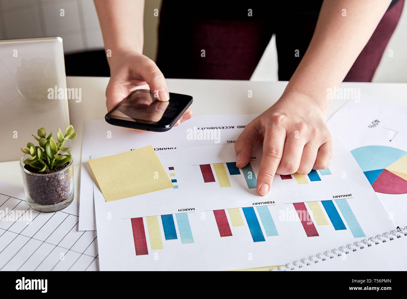 Close up of businesswoman analyzing data with smart phone. Desk of a young woman entrepreneur Stock Photo