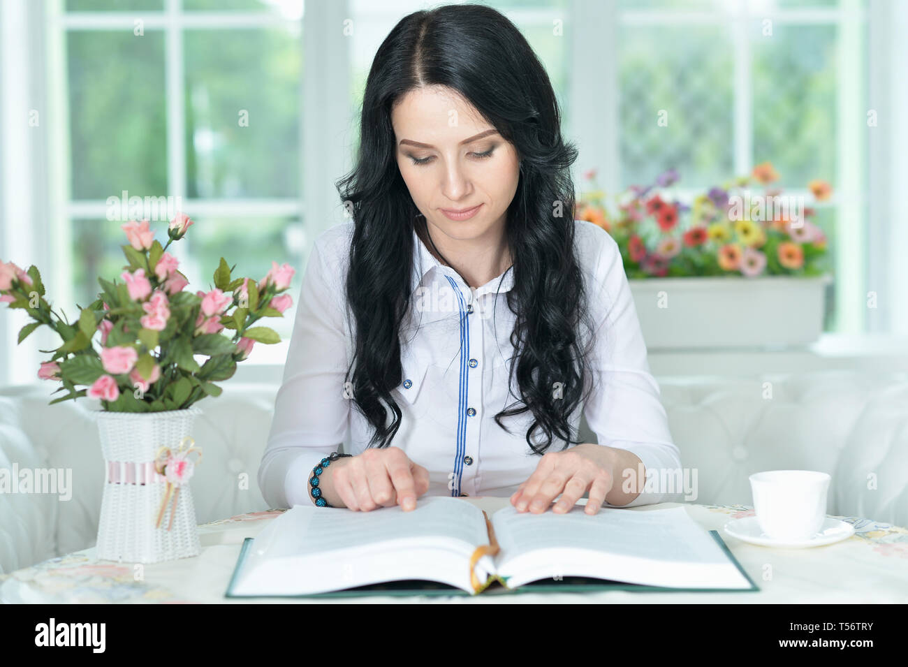 Beautiful young woman sitting at table with opened book Stock Photo - Alamy