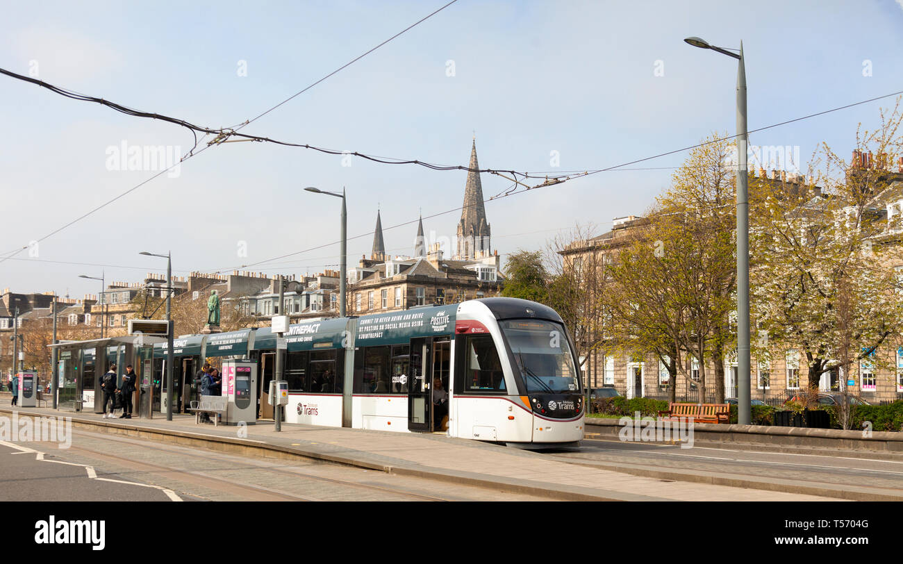 An Urbos 3 tram at the West End - Princes Street light railway station with Coates Terrace, the William Gladstone Monument and St Mary's Cathdral in t Stock Photo