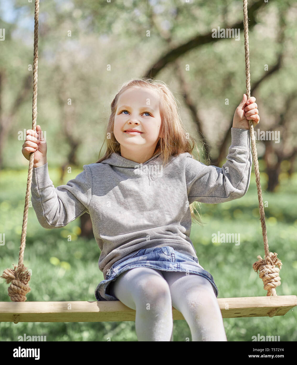smiling little girl sitting on a swing in the garden. the concept of ...