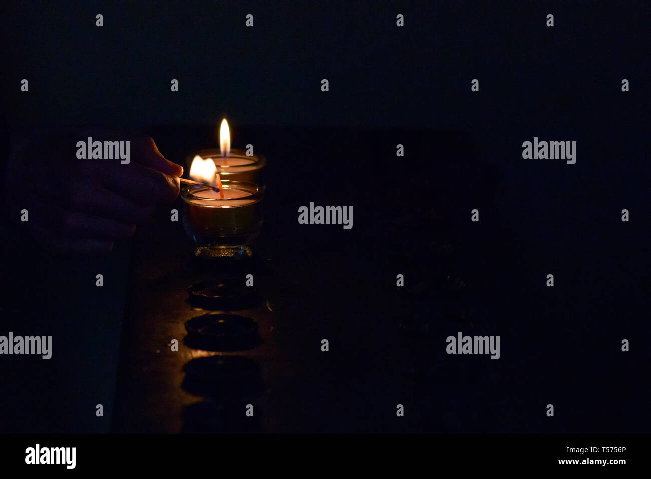 Lighting a votive candle in church on special candle holder. Senior