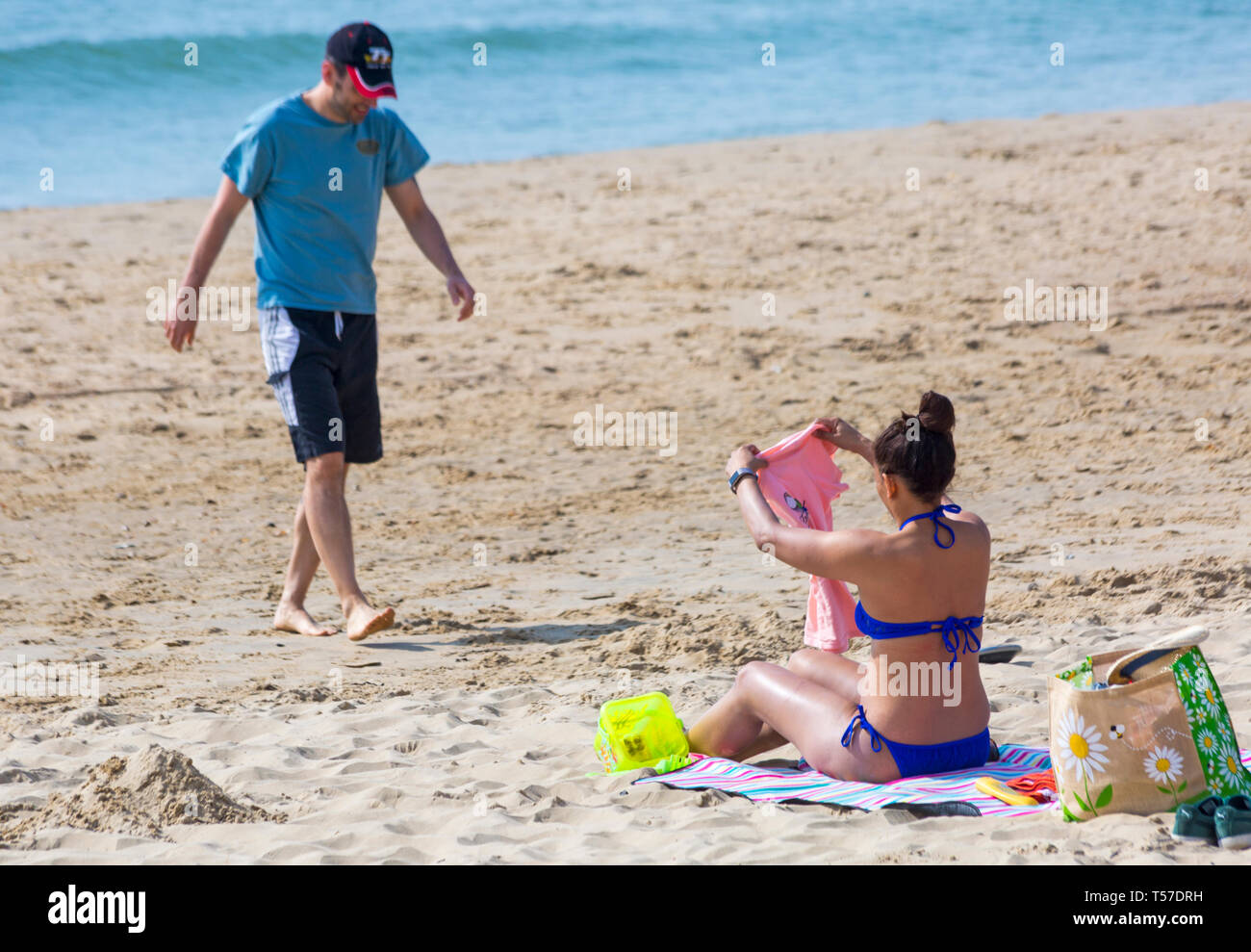 Bournemouth, Dorset, UK. 22nd Apr, 2019. UK weather: after a hazy start the glorious weather continues with hot and sunny weather, as beachgoers head to the seaside to enjoy the heat and sunshine at Bournemouth beaches on Easter Monday before the weather changes and the return to work. Woman in blue bikini sunbathing at the beach with man walking towards her. Credit: Carolyn Jenkins/Alamy Live News Stock Photo