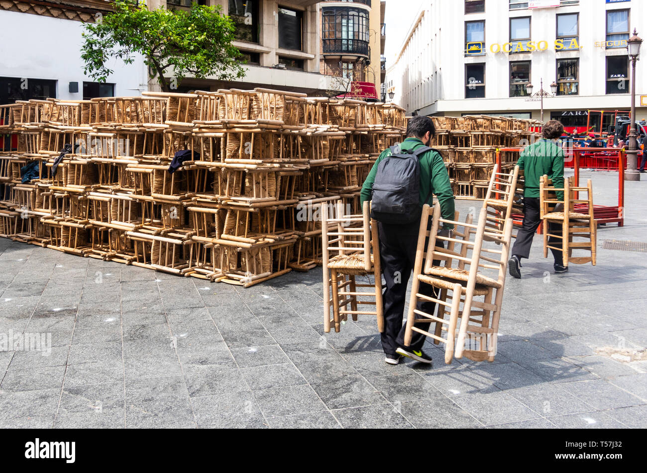 Two men moving wooden chairs in Seville Stock Photo Alamy