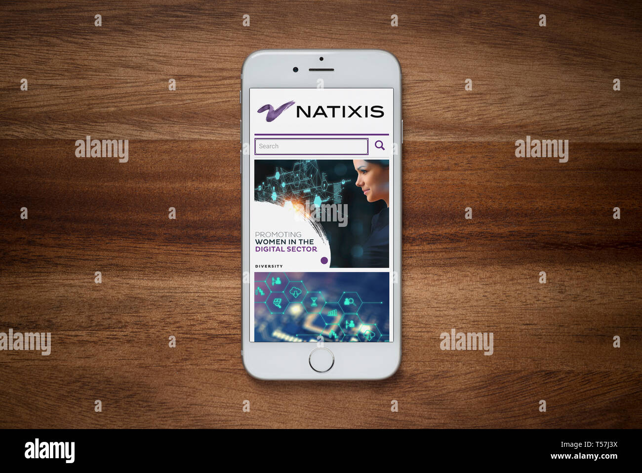 An iPhone showing the Natixis website rests on a plain wooden table (Editorial use only). Stock Photo