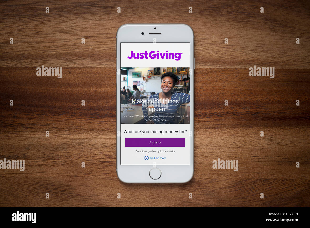 An iPhone showing the JustGiving website rests on a plain wooden table (Editorial use only). Stock Photo