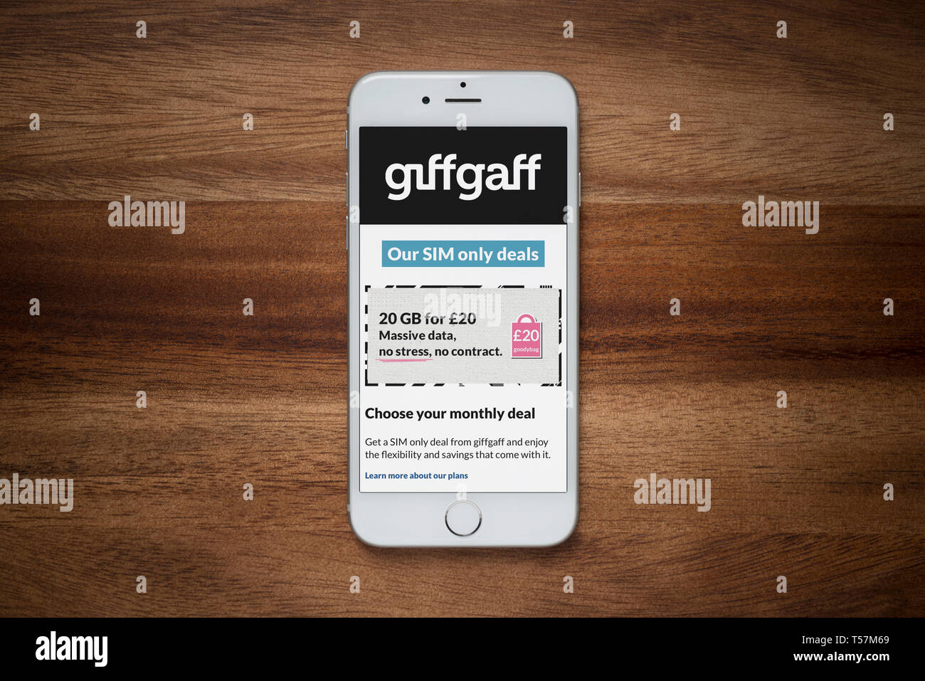 An iPhone showing the Giffgaff website rests on a plain wooden table (Editorial use only). Stock Photo
