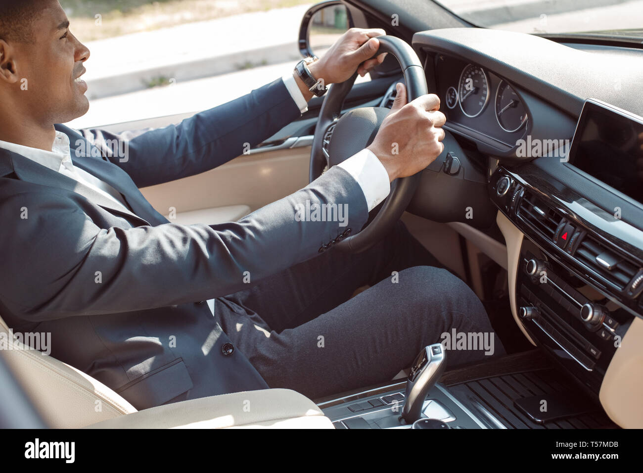 Young african american businessman driver sitting inside the car driving holding steering wheel smiling joyful side view Stock Photo