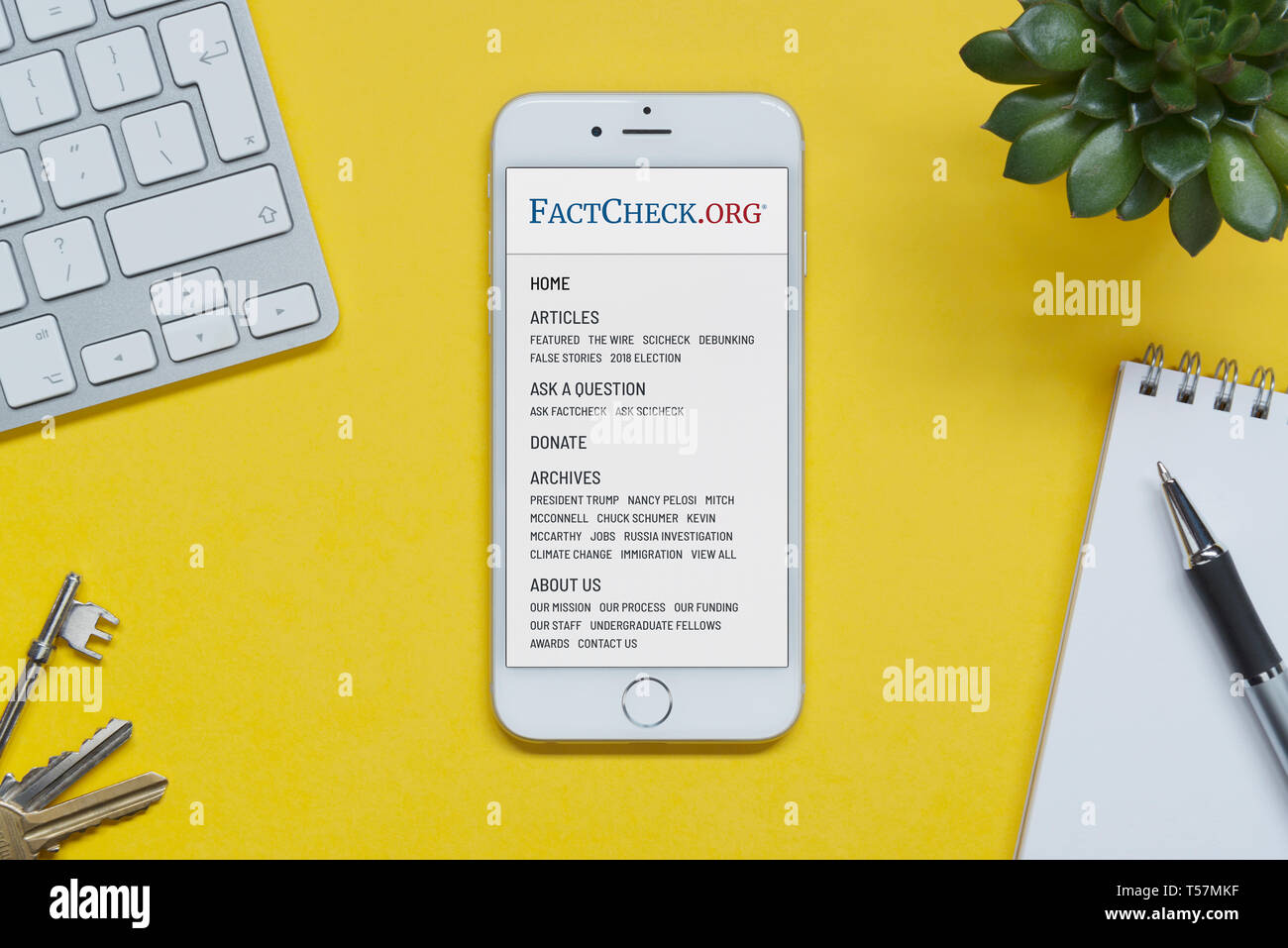 An iPhone showing the FactCheck.org website rests on a yellow background table with a keyboard, keys, notepad and plant (Editorial use only). Stock Photo