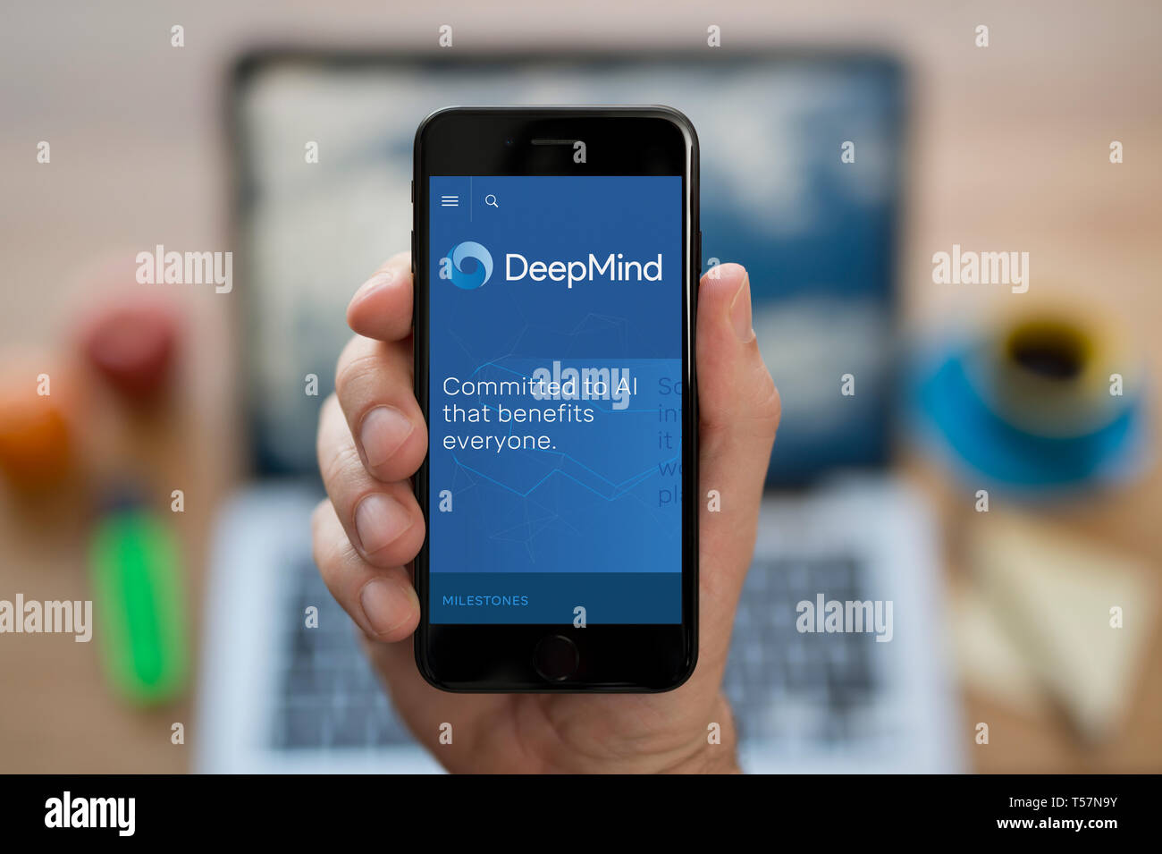 A man looks at his iPhone which displays the DeepMind logo (Editorial use only). Stock Photo