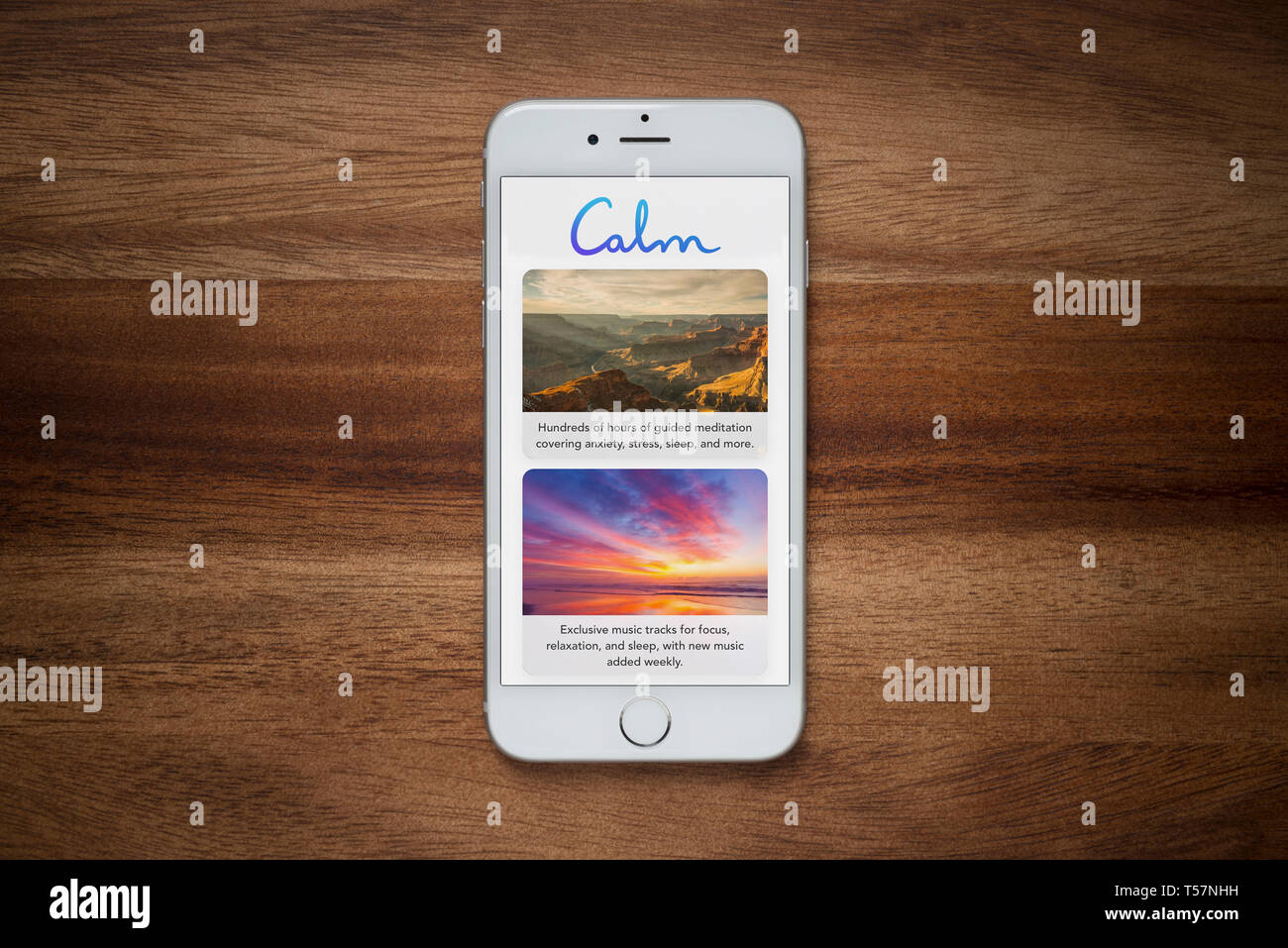 An iPhone showing the Calm app rests on a plain wooden table (Editorial use only). Stock Photo