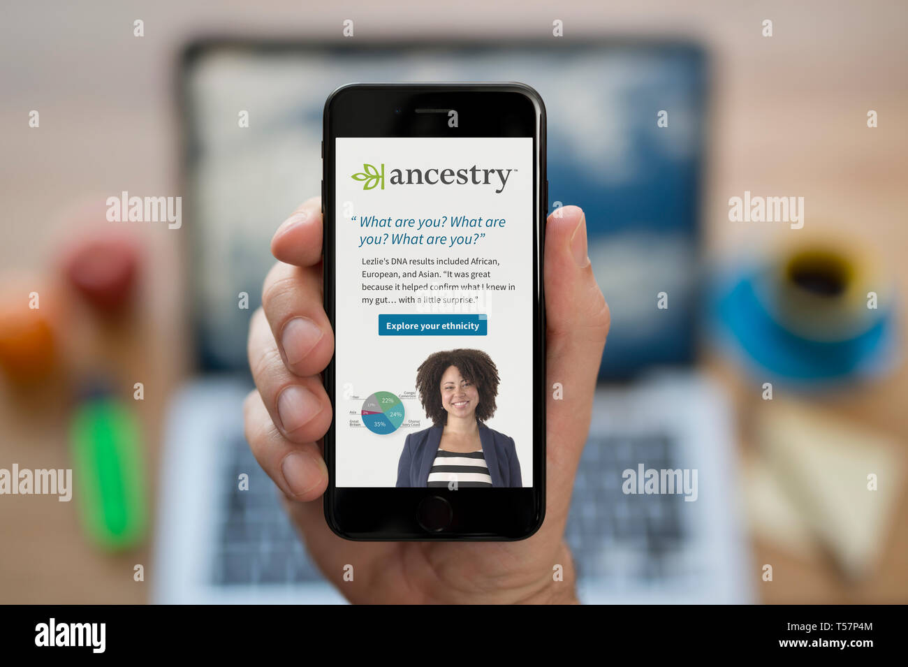 A man looks at his iPhone which displays the Ancestry logo (Editorial use only). Stock Photo